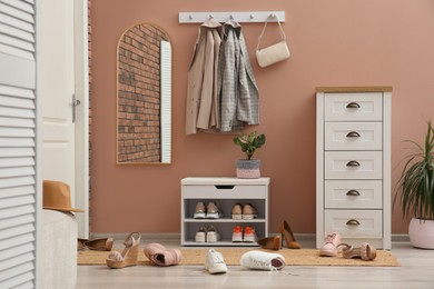Photo of Stylish furniture and scattered shoes on floor in hall