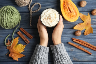 Woman holding glass with pumpkin spice latte on wooden background, top view