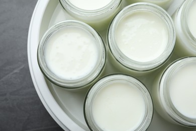 Photo of Modern yogurt maker with full jars on dark grey table, top view