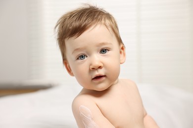 Cute little baby with moisturizing cream on body indoors