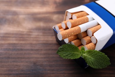 Photo of Pack of menthol cigarettes and mint leaves on wooden table, closeup. Space for text