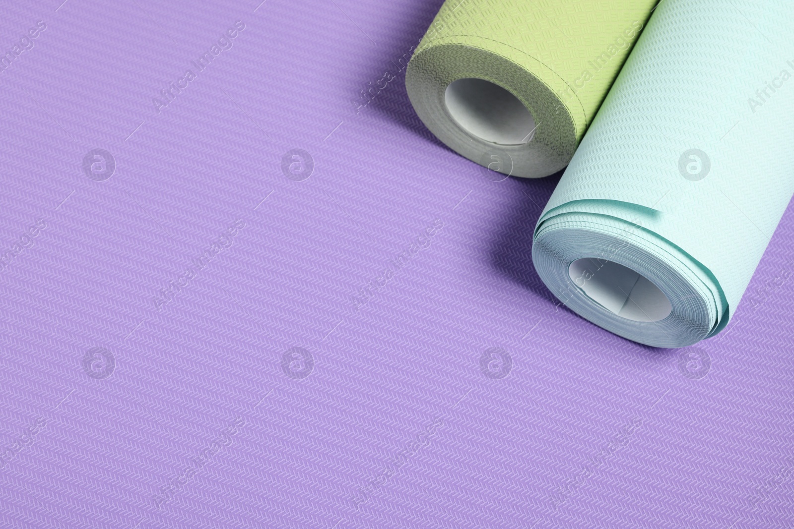 Photo of Two colorful wallpaper rolls on violet sample, above view. Space for text