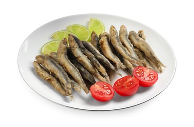 Plate with delicious fried anchovies, lime slices and tomatoes on white background