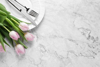 Photo of Stylish table setting with cutlery and tulips on white marble background, flat lay. Space for text