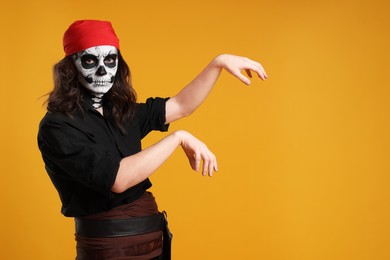 Man in scary pirate costume with skull makeup posing on orange background, space for text. Halloween celebration