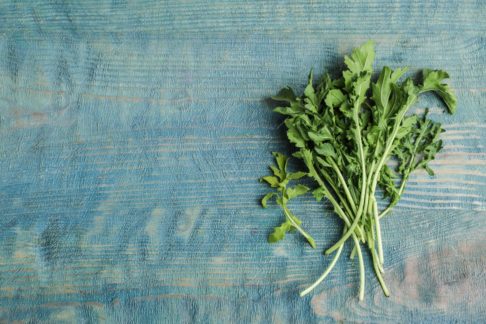 Photo of Fresh arugula on blue wooden table, flat lay. Space for text