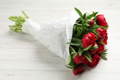 Beautiful bouquet of red peony flowers wrapped in paper on white wooden table