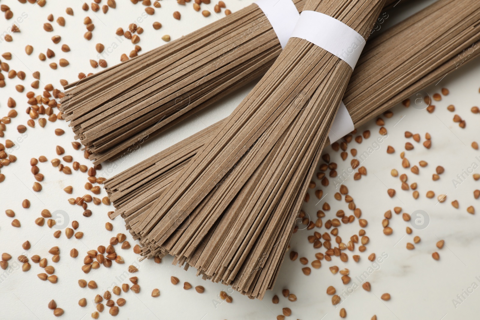 Photo of Uncooked buckwheat noodles (soba) and grains on white marble table, flat lay