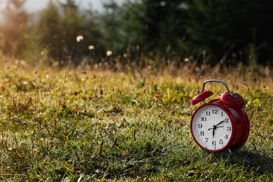 Red alarm clock on grass outdoors in morning, space for text