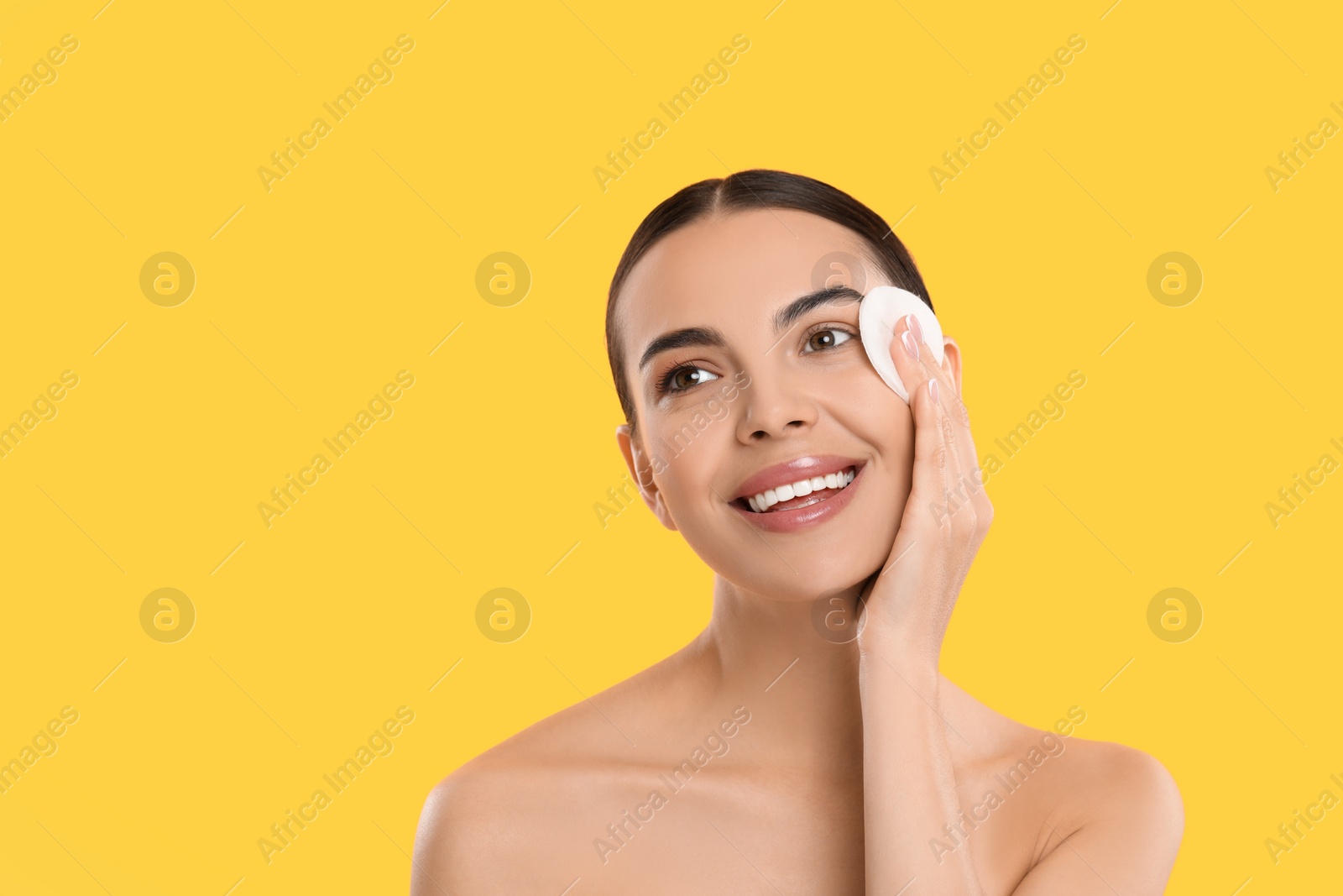 Photo of Beautiful woman removing makeup with cotton pad on yellow background. Space for text