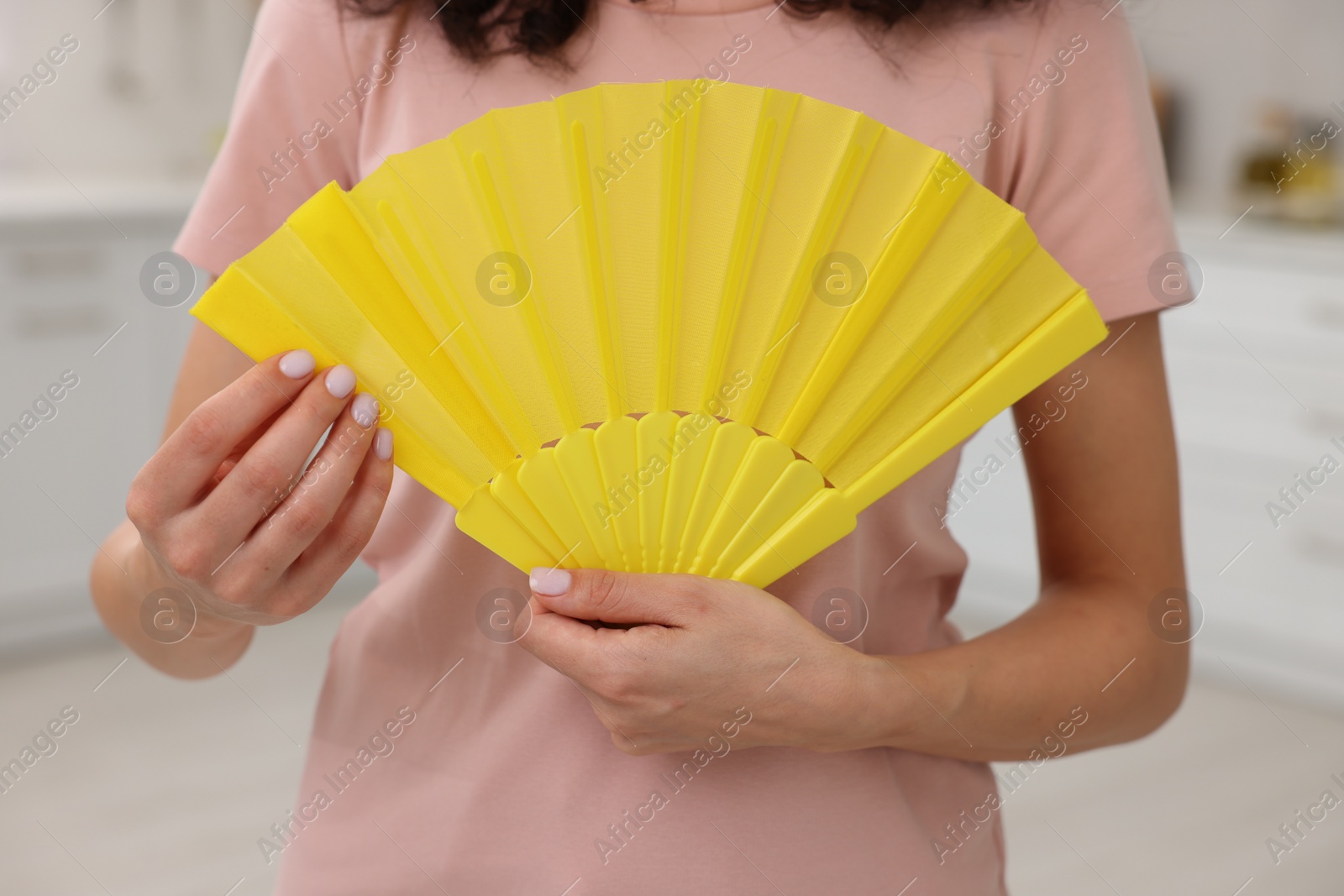 Photo of Woman with yellow hand fan indoors, closeup