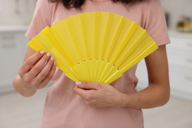 Photo of Woman with yellow hand fan indoors, closeup