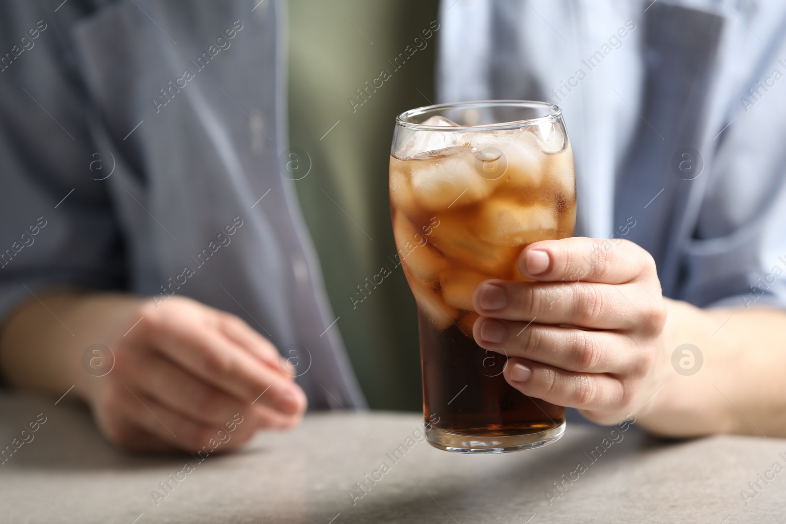 Photo of Woman holding glass of cola with ice at table, closeup