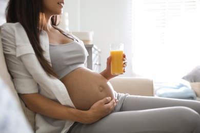 Photo of Young pregnant woman with glass of juice in living room, closeup. Taking care of baby health