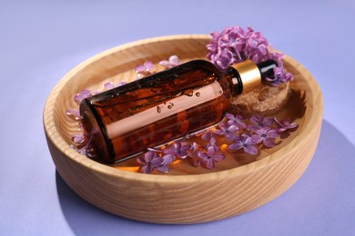 Bottle with essential oil, lilac flowers and water in bowl on violet background