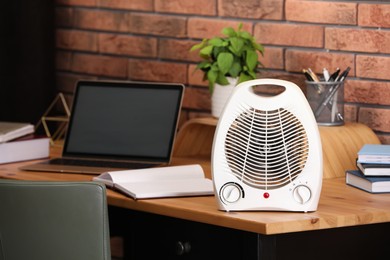 Photo of Modern electric fan heater near laptop and notebooks on wooden table in office