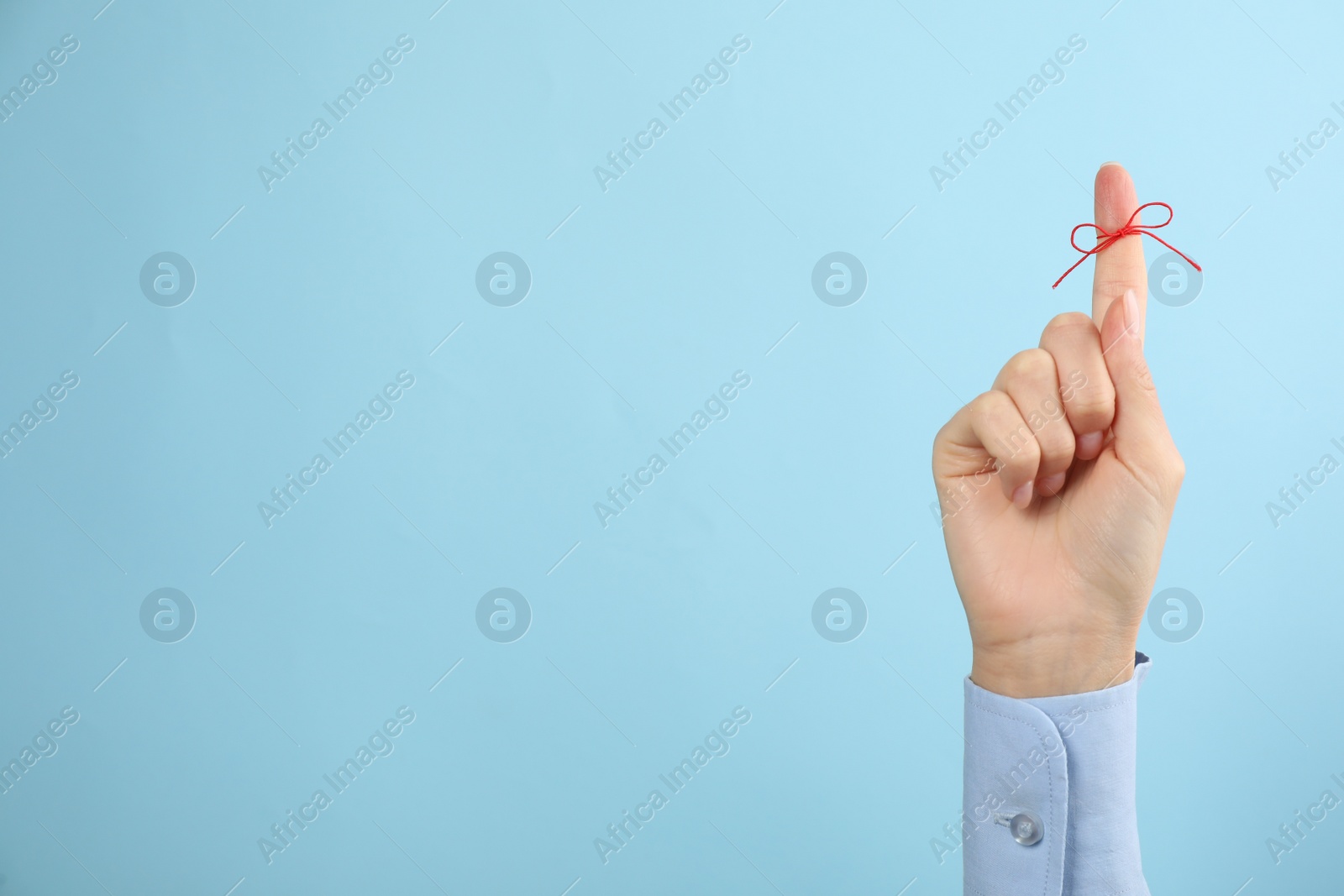 Photo of Woman showing index finger with tied red bow as reminder on light blue background, closeup. Space for text