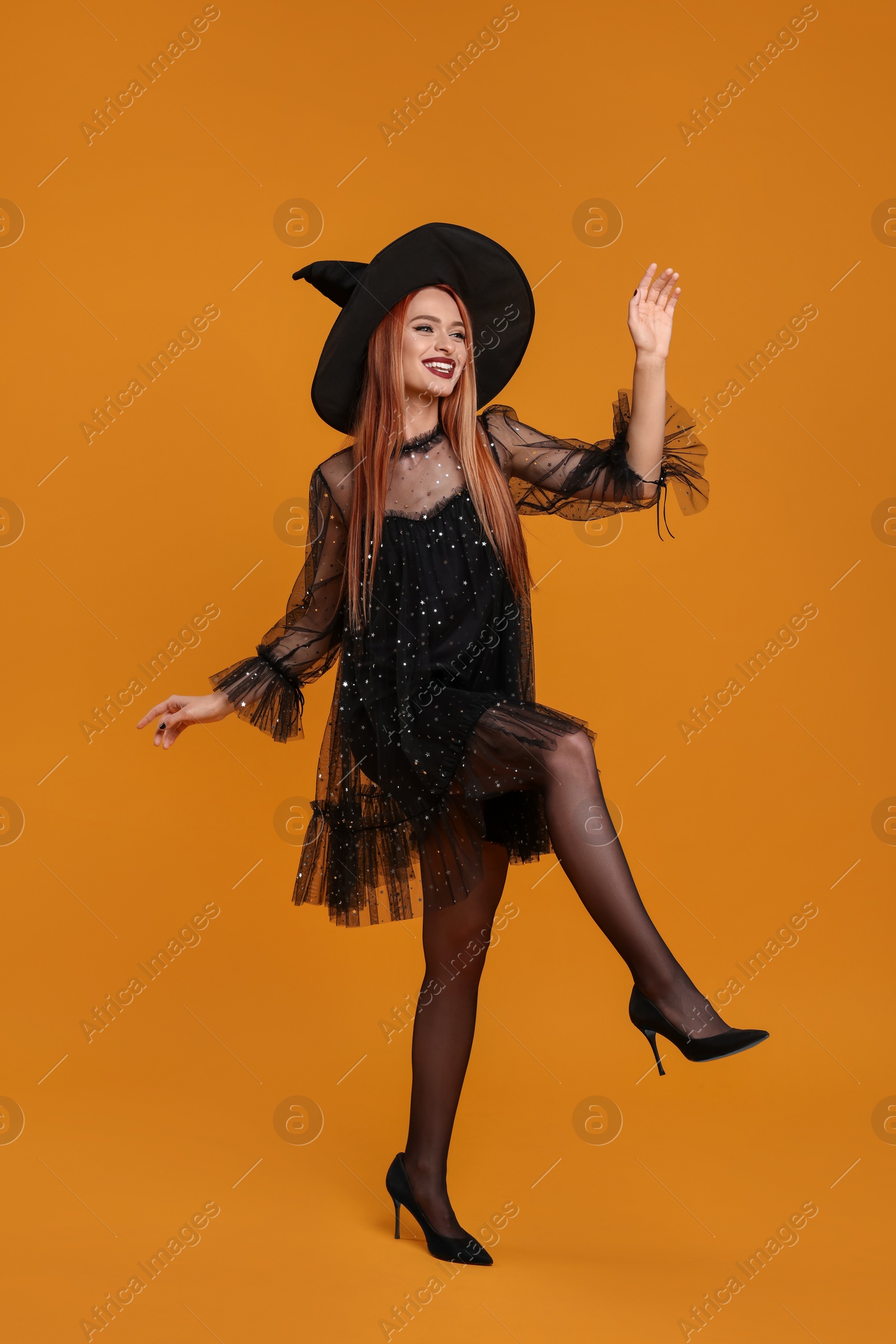 Photo of Happy young woman in scary witch costume posing on orange background. Halloween celebration