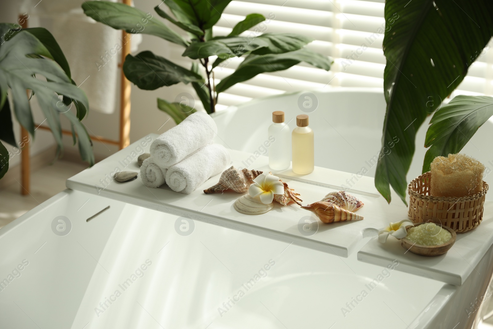 Photo of Bath tray with spa products, towels and shells on tub in bathroom