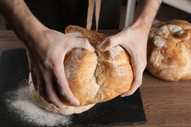 Male baker holding loaf of bread over table, closeup