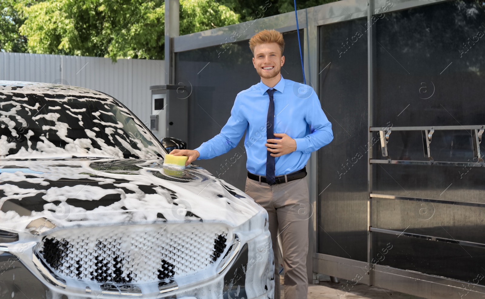 Photo of Businessman cleaning auto with sponge at self-service car wash