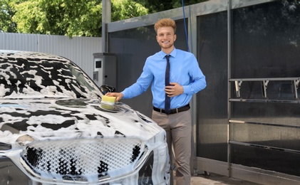 Photo of Businessman cleaning auto with sponge at self-service car wash