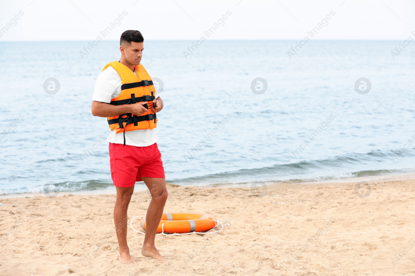 Photo of Handsome male lifeguard putting on life vest at sandy beach