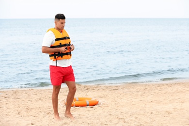 Handsome male lifeguard putting on life vest at sandy beach
