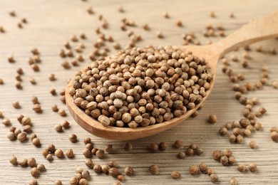 Spoon with dried coriander seeds on wooden table, closeup