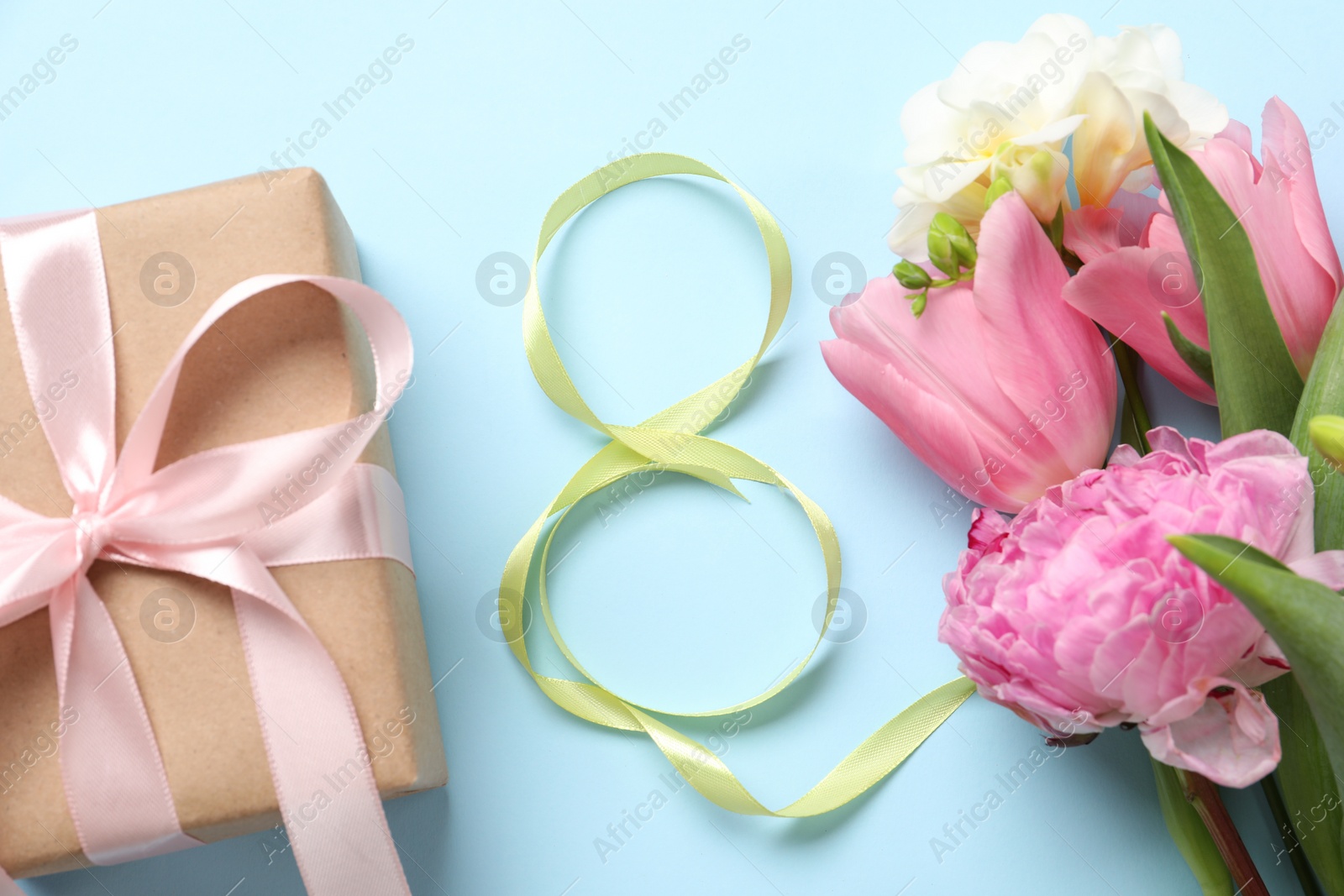 Photo of 8th of March greeting card design with green ribbon, present and beautiful flowers on light blue background, flat lay. International Women's day