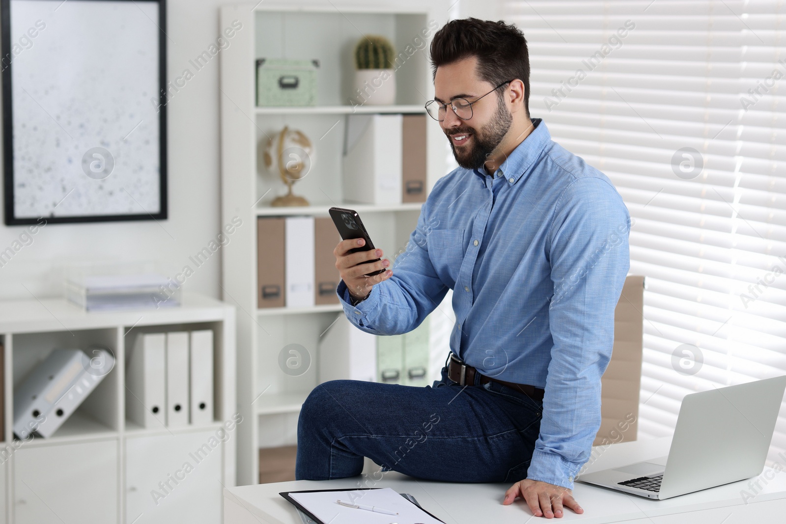 Photo of Happy young man using smartphone in office