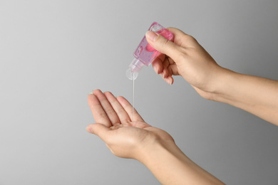 Woman applying antiseptic gel onto hand against light grey background, closeup. Virus prevention