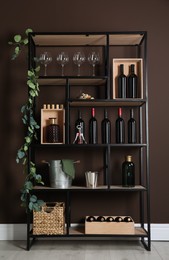 Rack with bottles of wine and glasses near brown wall