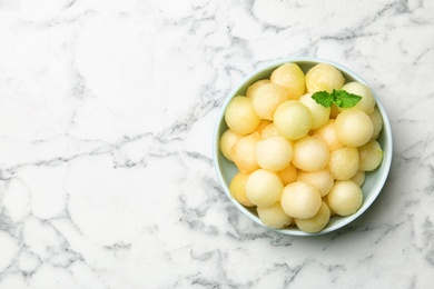 Photo of Plate of melon balls with mint on white marble table, top view. Space for text