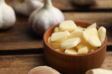 Photo of Fresh chopped garlic in bowl on wooden table, closeup. Organic product