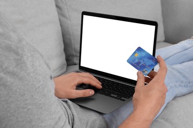 Photo of Man with credit card using laptop for online shopping on sofa, closeup