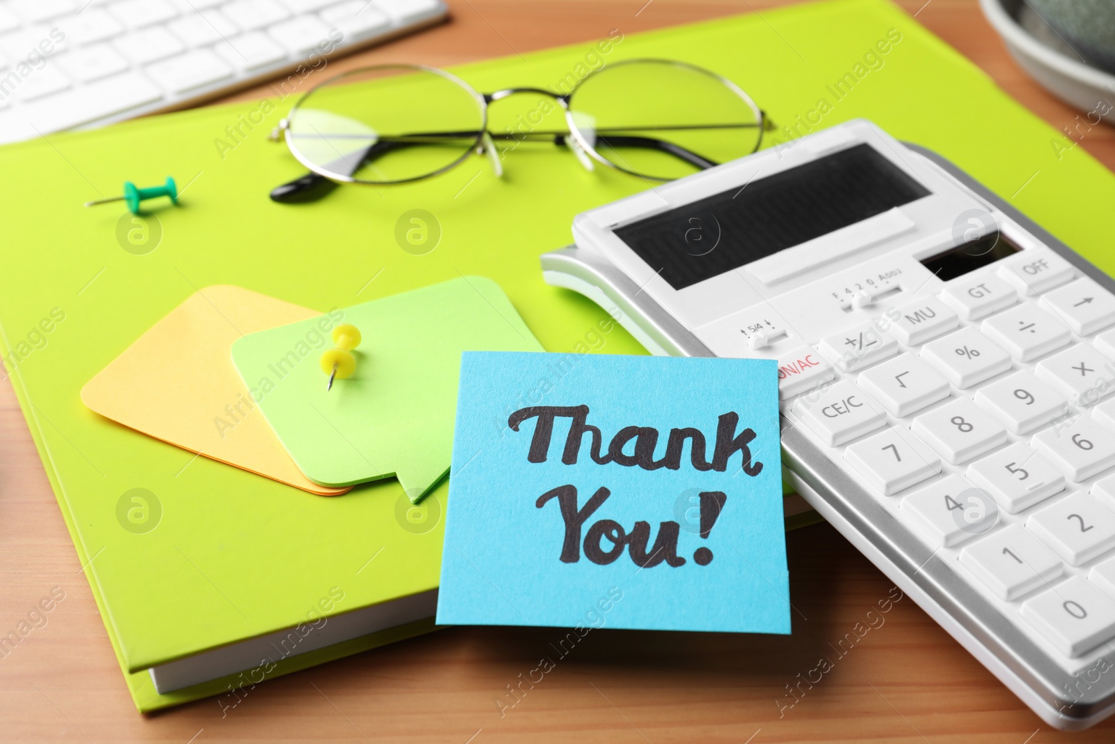 Photo of Light blue paper note with phrase Thank You, calculator and notebook on wooden table