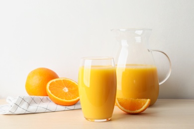 Photo of Glass and jug of orange juice and fresh fruits on wooden table