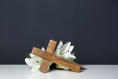 Photo of Composition with wooden cross and blossom lilies on table against color background