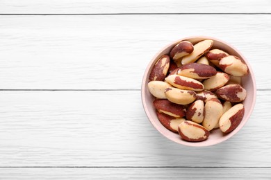 Photo of Bowl of delicious Brazil nuts on white wooden table, top view. Space for text