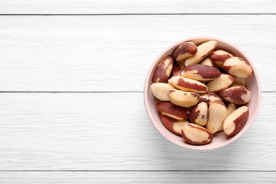 Bowl of delicious Brazil nuts on white wooden table, top view. Space for text