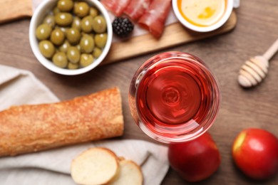 Photo of Glass of delicious rose wine and snacks on wooden table, flat lay