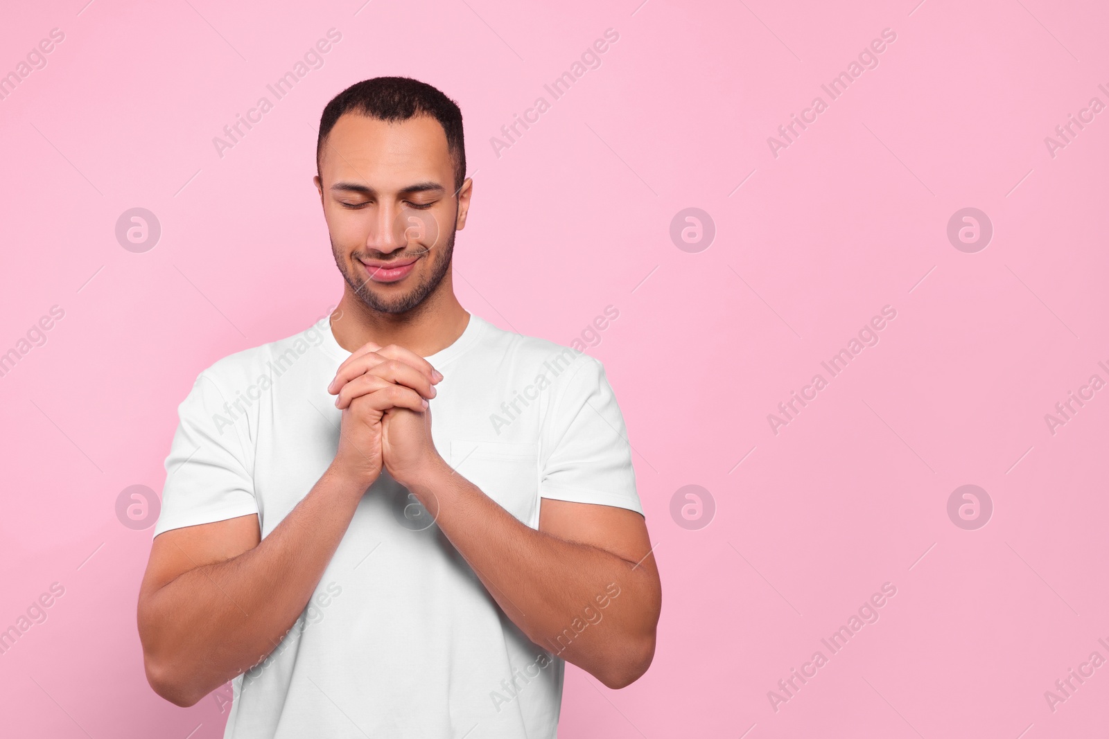 Photo of African American man with clasped hands praying to God on pink background. Space for text