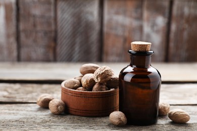 Photo of Bottle of nutmeg oil and nuts on wooden table