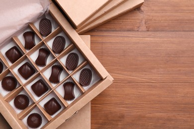 Photo of Many delicious chocolate candies in box on wooden table, top view and space for text. Production line
