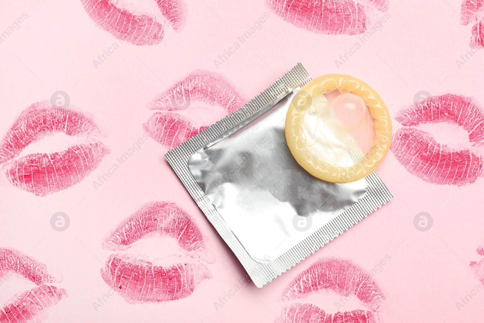 Photo of Condom with lipstick kiss marks on pink background, flat lay. Safe sex