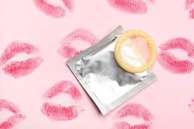 Photo of Condom with lipstick kiss marks on pink background, flat lay. Safe sex