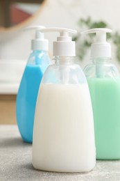 Photo of Dispensers of liquid soap on light grey table in bathroom