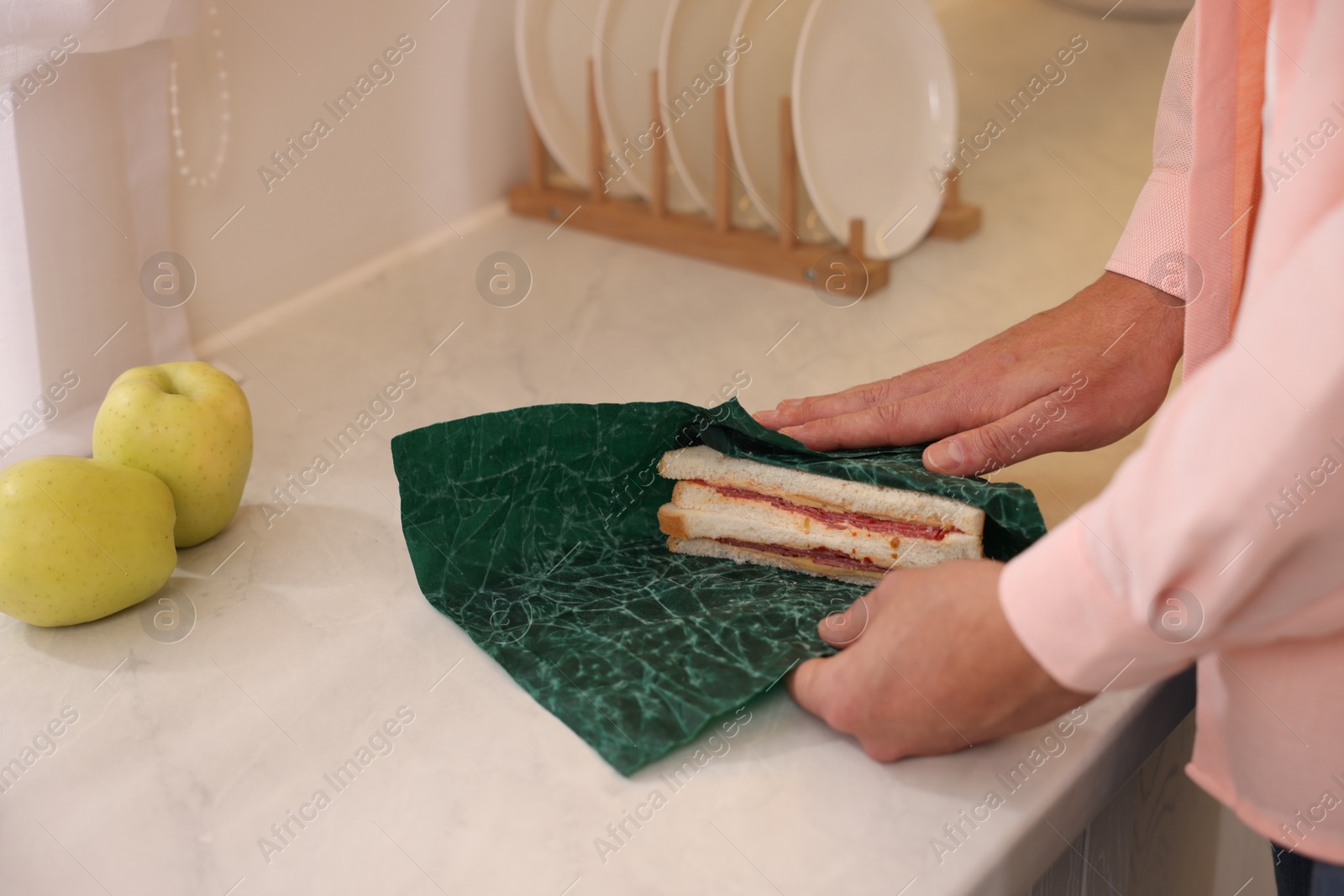 Photo of Man packing sandwich into beeswax food wrap at white countertop in kitchen, closeup