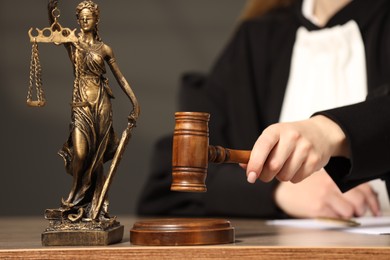 Judge striking mallet at wooden table indoors, selective focus. Figure of Lady Justice, closeup